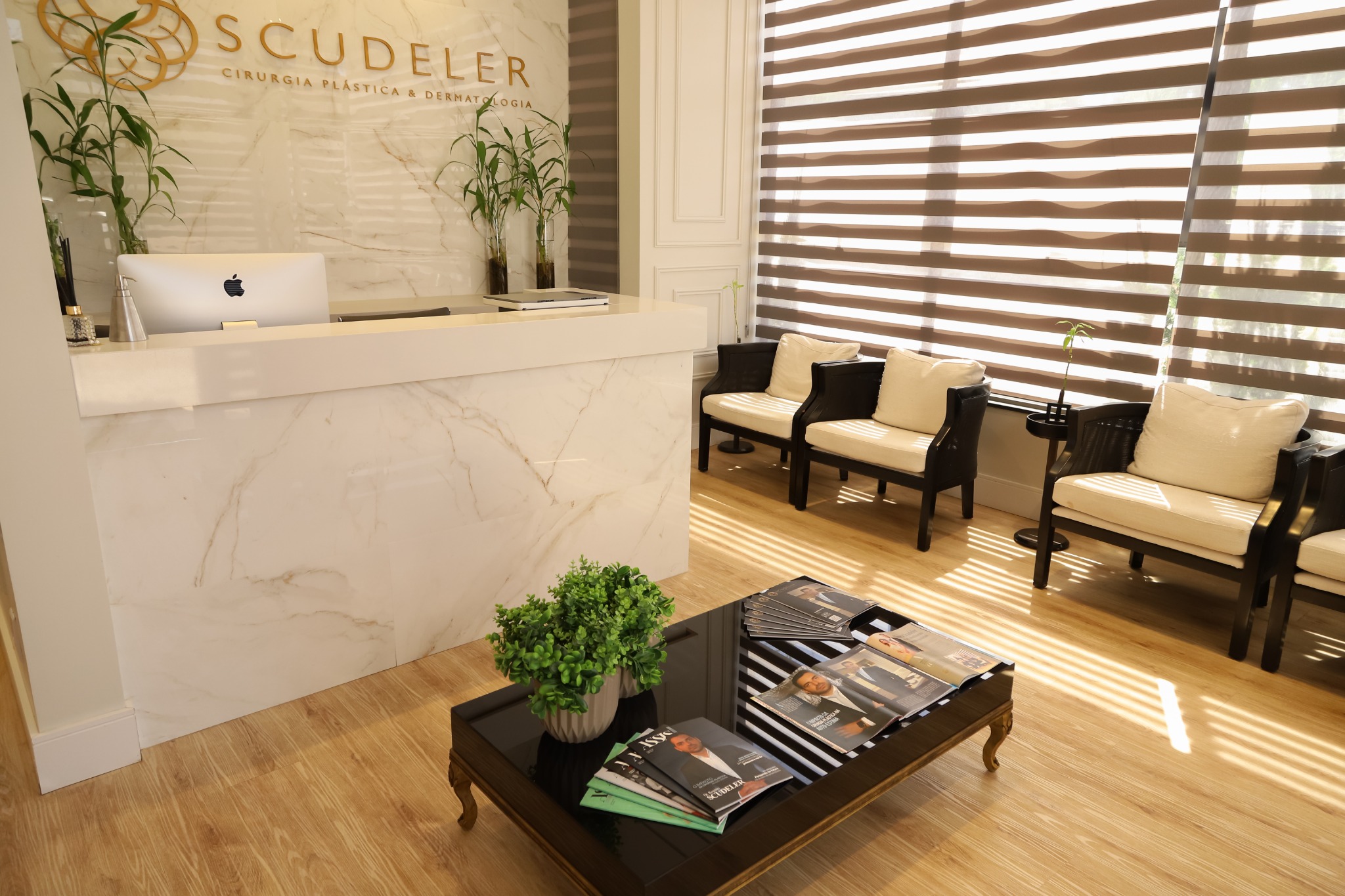 Recepção da Clínica Scudeler, em Assis, com a logomarca dourada, balcão em mármore e área de espera